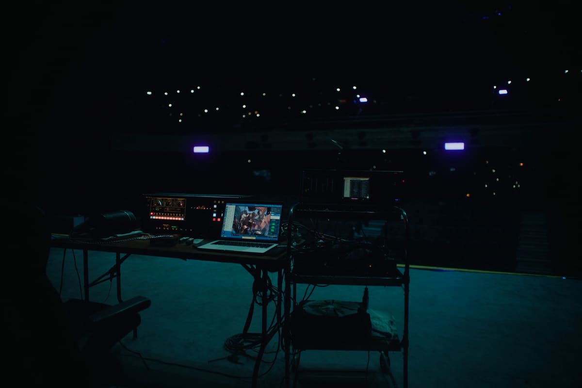 Puesto de producción al fondo de un auditorio a oscuras, con una notebook y una consola
